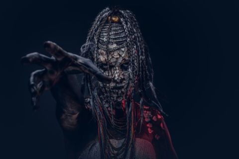 Personnage masqué aux dreadlocks et maquillage rituel dans l'atmosphère sombre de Vaudou