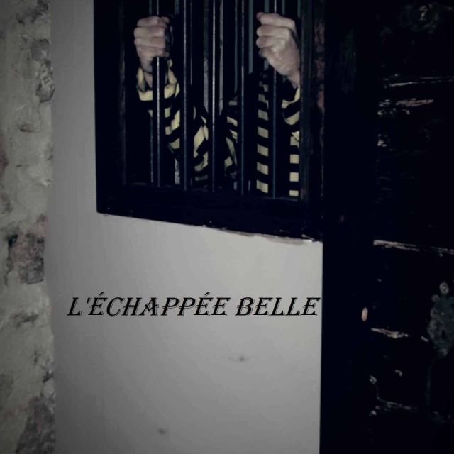 Couloir sombre avec barreaux de cellule et porte noire dans la salle Prison de L'ÉCHAPPÉE BELLE
