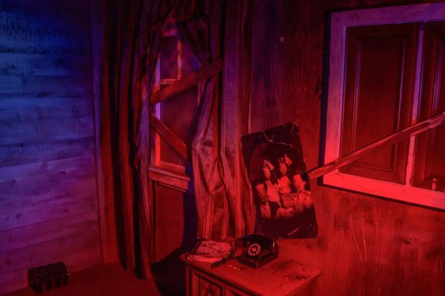 Décor industriel aux teintes rouge et bleu, téléphone rétro et objets sur établi dans The Nightmare