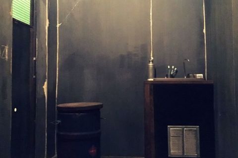 Cellule sombre avec murs gris, bureau en bois et objets dispersés chez Escape Max à Argenteuil