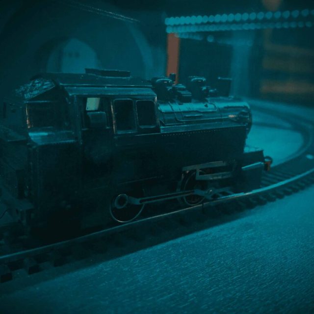 Maquette de locomotive à vapeur sur ses rails dans une lumière bleutée, salle Sherlock, One O'Clock