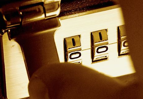 Main tournant les molettes d'un cadenas à code doré, visuel de L'Autre Monde, escape game à Bergerac
