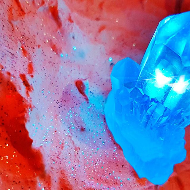 Cristal bleu lumineux posé sur une roche rouge, salle Mirage chez Escape Time à Barjouville