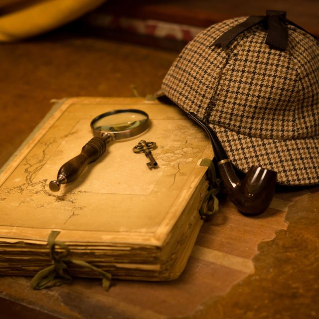 Loupe, clé dorée, journal ancien et casquette de détective sur table usée