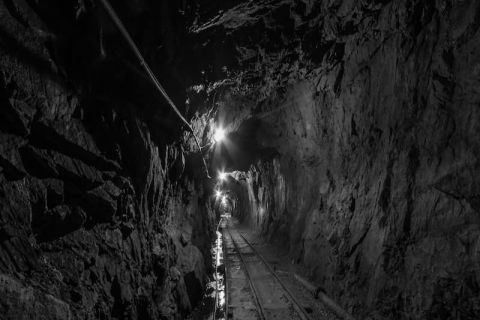 Galerie de mine en noir et blanc, rails et lampe au fond, salle La mine aux secrets chez Mindtrap à Serris