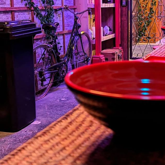 Grand bol rouge laqué sur un comptoir, poubelle et plantes grimpantes, lumière violette, salle Mission Tokyo à Angers