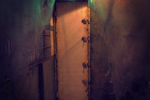 Couloir souterrain délabré aux murs rouillés, porte métallique massive verrouillée chez L'Abattoir