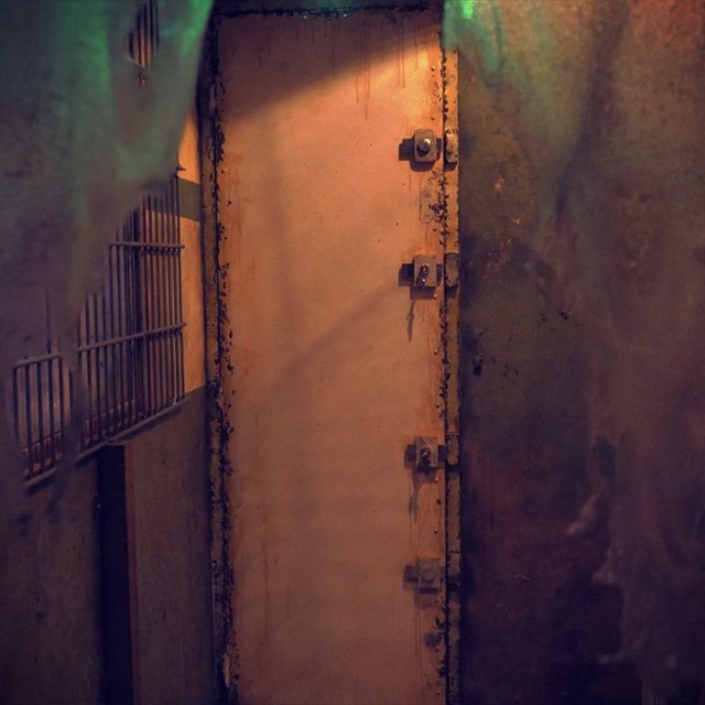 Couloir souterrain délabré aux murs rouillés, porte métallique massive verrouillée chez L'Abattoir