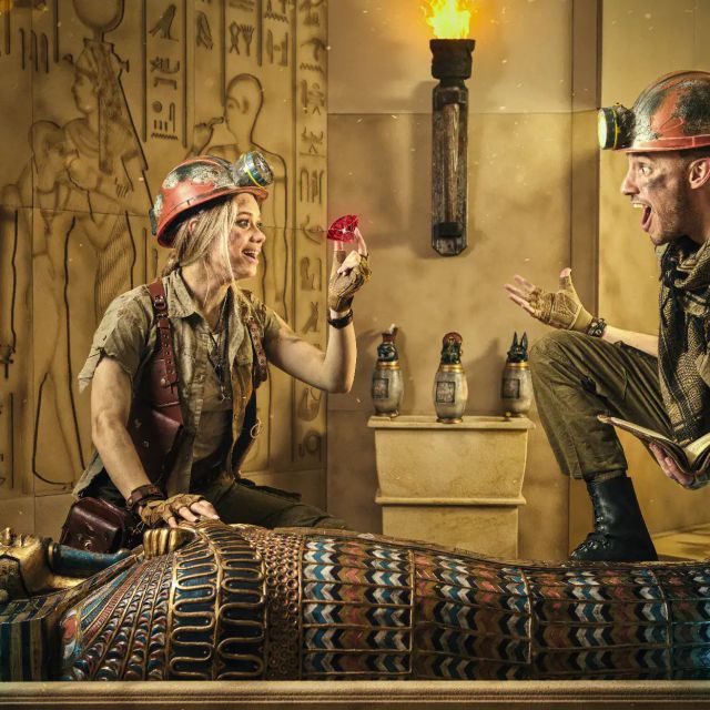 Explorateurs assis sur un sarcophage peint, un joyau rouge à la main, Le Trésor de Bastet
