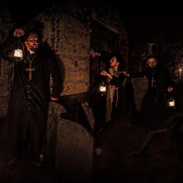 Groupe en costumes sombres dans un cimetière souterrain aux tombes éclairées à la bougie