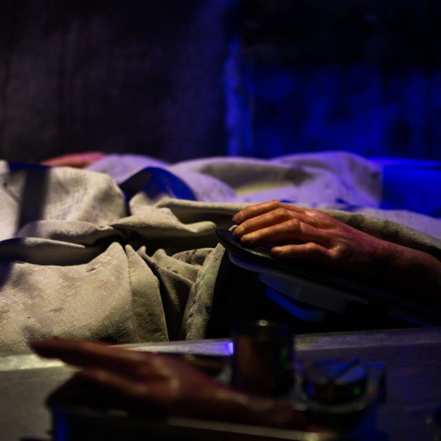 Main dépassant d'un drap sous une lumière bleue, décor d'une salle de Rashomon Escape