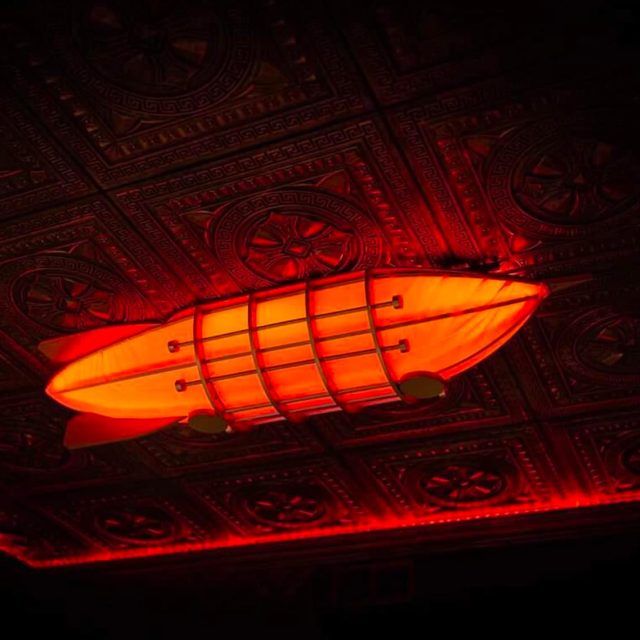 Plafond ornementé portant un dirigeable lumineux orange, salle Sherlock Holmes chez Freeing à Saint-Maximin