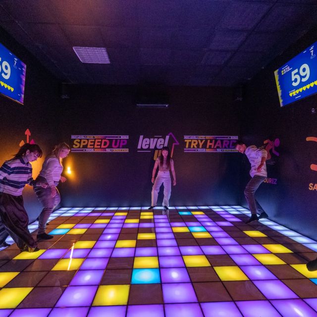 Groupe de joueurs dansant sur un sol lumineux multicolore sous des écrans à 59, salle Level UP chez Le Voyage Heure