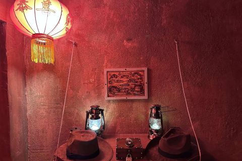 Lampion rouge, carte encadrée, lanternes et chapeaux d'aventurier sur un mur rouge, salle Le temple sacré chez Fun Room à Lons
