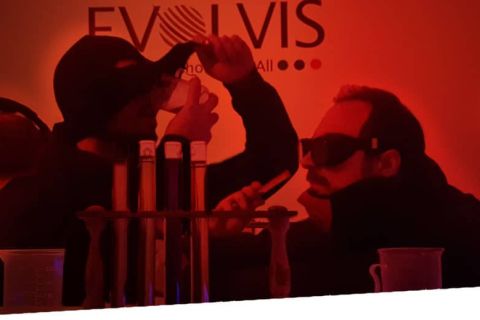 Silhouettes en lunettes devant des tubes à essai sous une lumière rouge, salle Mission Evolvis chez Immersia