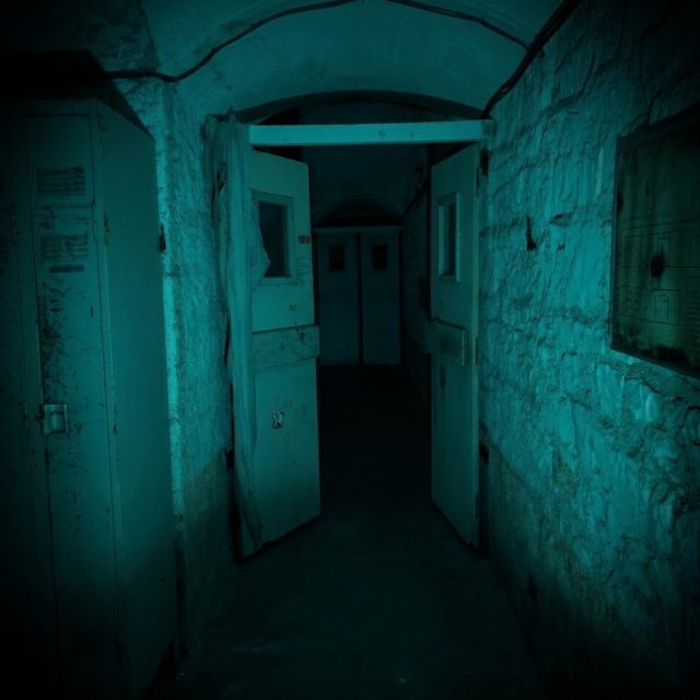 Couloir d'asile délabré aux murs turquoise, portes ouvertes dans l'obscurité de la salle