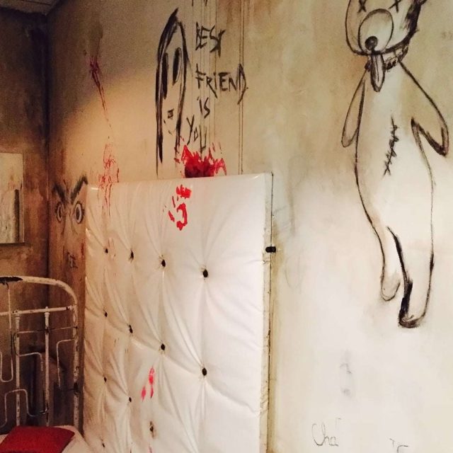 Chambre d'asile aux murs souillés, dessins enfantins et traces rouges sanglantes