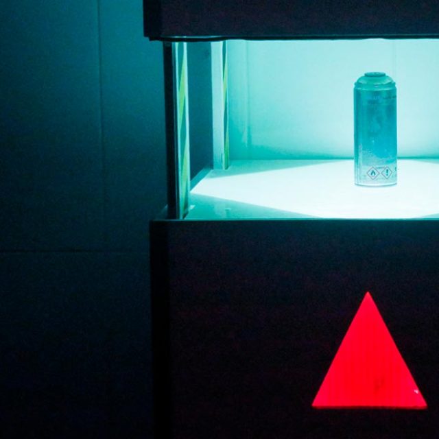 Vitrines illuminées en bleu turquoise avec cylindre et triangle rouge dans Time Lab