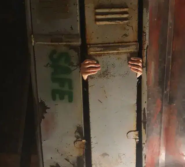 Mains de joueur écartant des portes métalliques rouillées dans un décor d'horreur