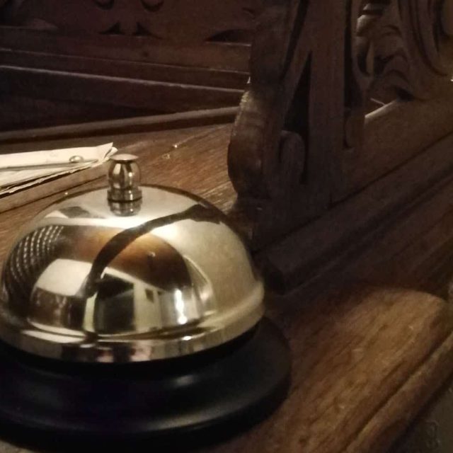 Sonnette de réception dorée sur comptoir en bois, décor d'hôtel à L'Hôtel des oubliés