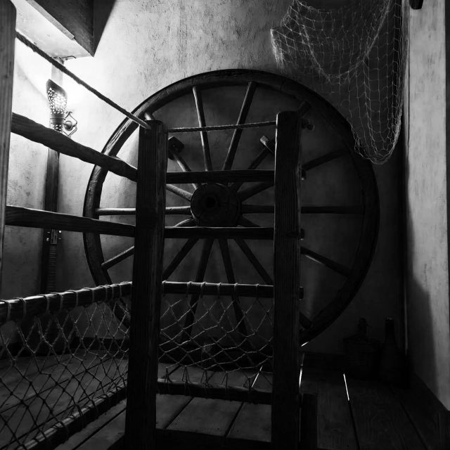 Cage et roue de bois dans un couloir en noir et blanc, salle La taverne de Malobid à Bourgoin-Jallieu