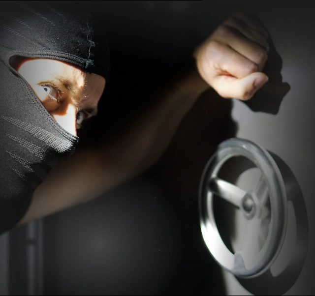 Braqueur masqué manipulant un volant de coffre-fort dans l'obscurité, ambiance de braquage