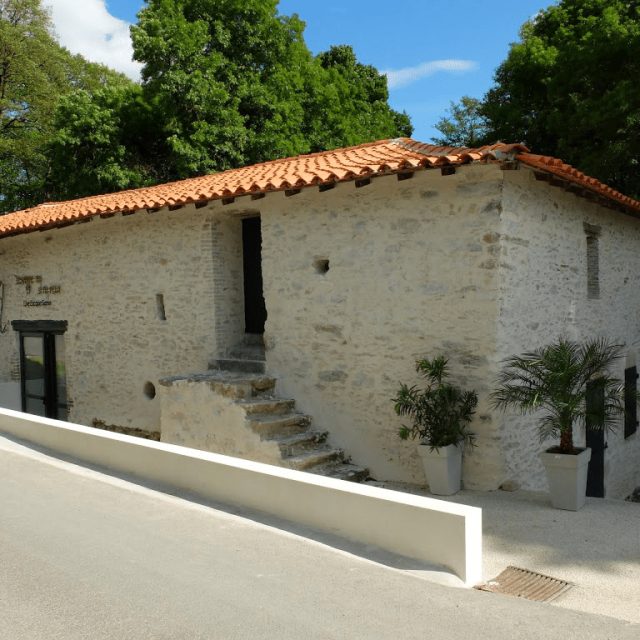Bâtisse blanche aux murs de pierre et toit de tuiles rouges, entourée de verdure
