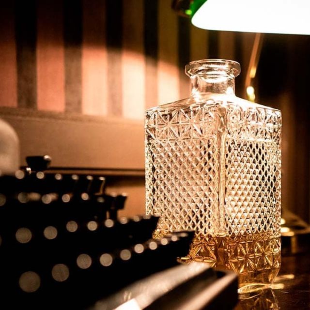 Carafe en cristal, cendrier et machine à écrire sous une lampe verte, salle Sunhill Hotel chez Escape Time à Laval