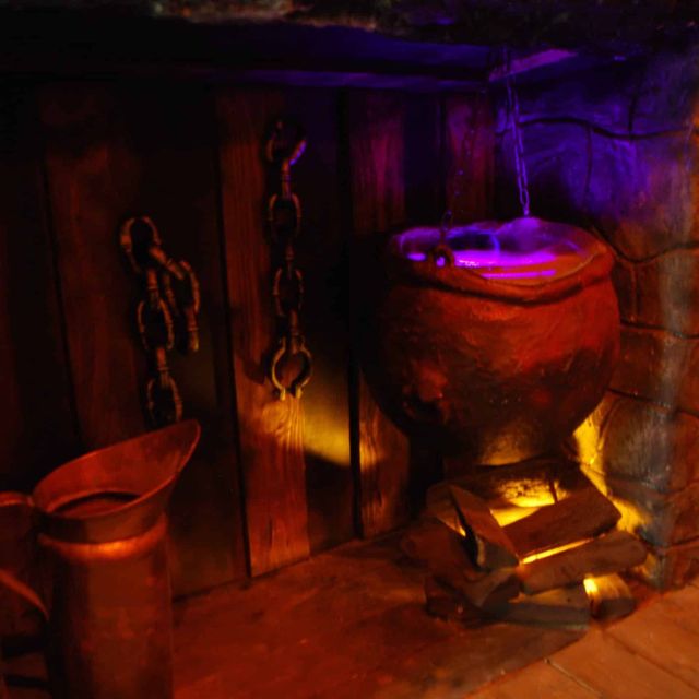 Décor souterrain aux chaînes et cauldron illuminé en rouge et bleu chez Le Défi des Ducs