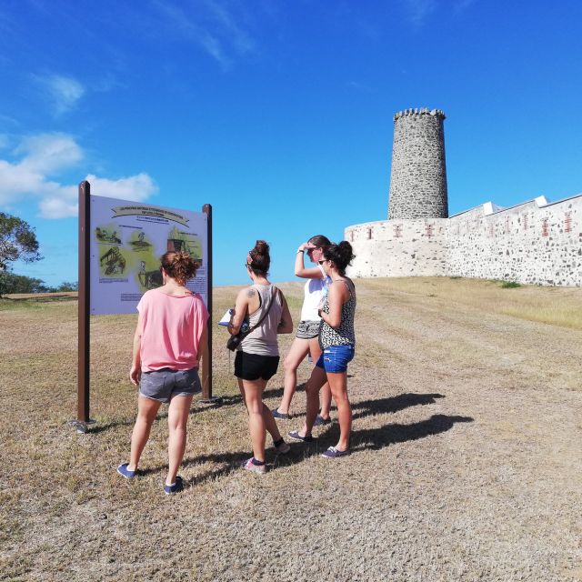 Visiteurs devant un panneau d'information près d'une tour ronde et de remparts, circuit La Grande Vadrouille, Fort Teremba