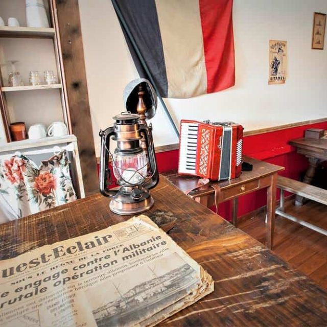 Intérieur d'époque avec drapeau français, journal, accordéon et lampe à huile chez BREIZH ESCAPE