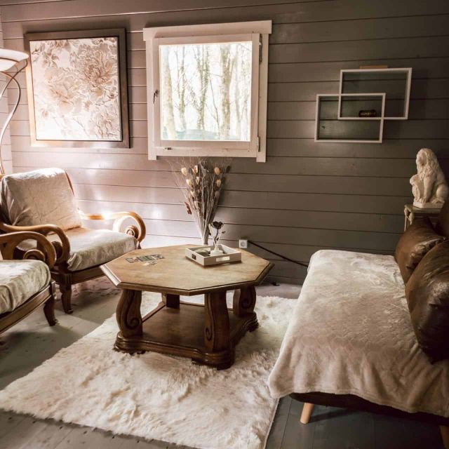 Salon de cabane en bois avec fauteuils, table basse ronde et tapis de fourrure clair, salle Cabane Yavana à Saint-Évarzec