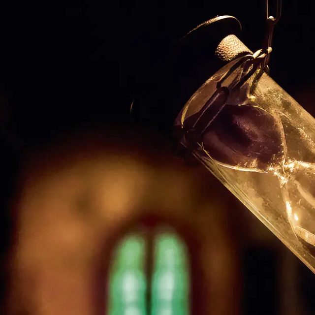 Sablier suspendu dans l'obscurité devant une petite fenêtre verte, salle Le donjon de l'alchimiste à Saint-Herblain