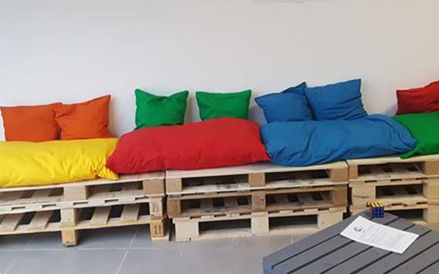 Banquette de palettes à coussins jaunes, rouges, verts et bleus devant un mur blanc, enseignes Cinsens Escape Game