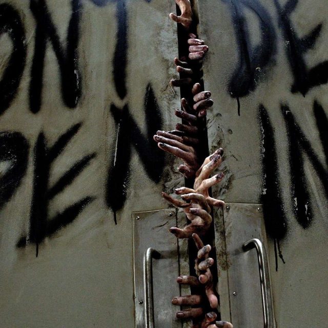 Mur dégradé et mains émergeant d'une surface, ambiance sombre et horrifique dans Walking Dead