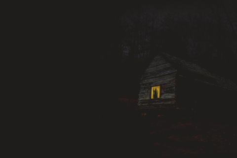 Maison sombre et isolée la nuit, fenêtre éclairée jaune, ambiance d'horreur chez Planet Experiences