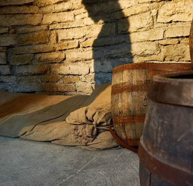 Barils et chaînes contre mur de pierre dans la salle Le Masque de Fer