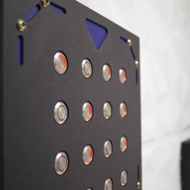 Panneau de commande noir avec boutons illuminés rouges et bleus dans LIVE Corp. Escape Game à Montpellier