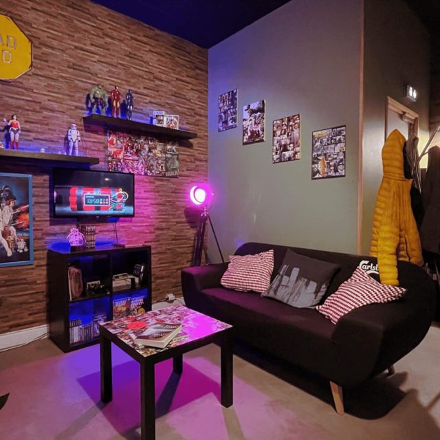 Salon gaming aux néons roses et bleus, murs en brique, écrans, figurines et costumes jaunes dans la salle 404 Hacker not found