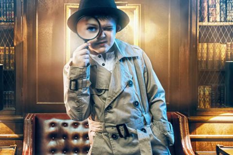 Enfant en trench et chapeau de détective regardant à travers une loupe, salle Le musée hanté chez Kid'Scape à Beynost
