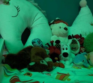 Peluches et coussins éclairés d'une lumière verte sur un lit, enseigne Pont'O Secret à Pont-Audemer