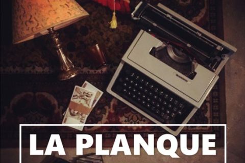 Machine à écrire, lampe et papiers sur un tapis, titre La Planque en lettres blanches, salle La Planque