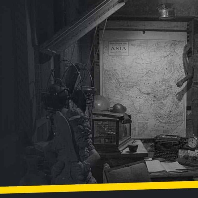 Bureau d'enquêteur années 1940 avec carte d'Asie, machine à écrire et ventilateur vintage dans la salle