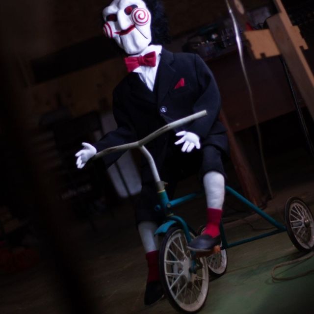Mannequin en costume formel sur tricycle dans décor sombre de SAW chez Dream Studio