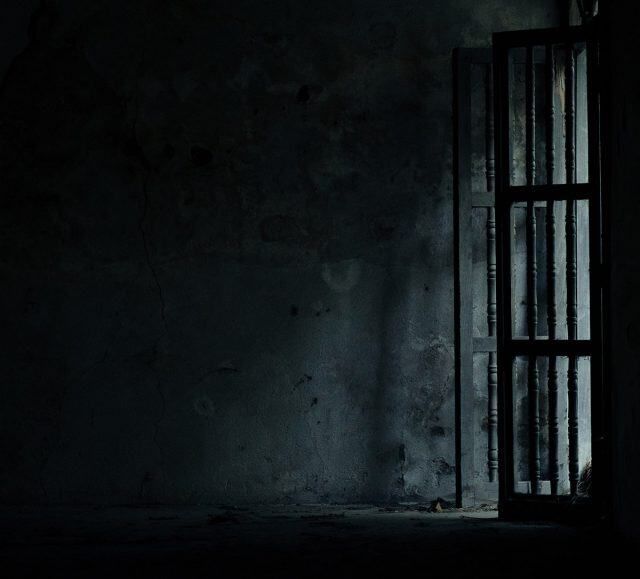 Pièce très sombre avec une porte à barreaux sur la droite, salle Sacrifice chez One O'Clock