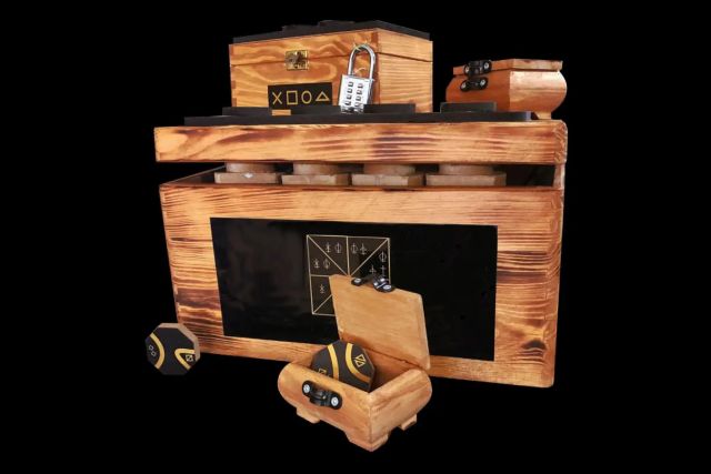 Coffre en bois flammé avec cadenas à code et petites boîtes sur fond noir, salle La Pirate Box chez A Maze In à Strasbourg