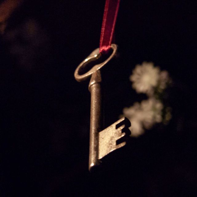 Clé ancienne à ruban rouge suspendue dans le noir, salle Au pays des merveilles chez Locked Time à Marseille