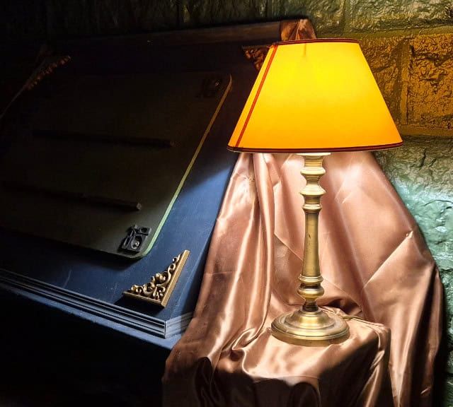 Lampe à abat-jour orange sur un drap rose devant un mur de pierre, salle Les sorciers de Calador chez Légendes Escape