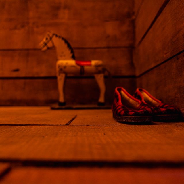 Cheval à bascule et chaussures rouges dans une pièce de bois orangée, salle La cabane dans les bois à Laxou