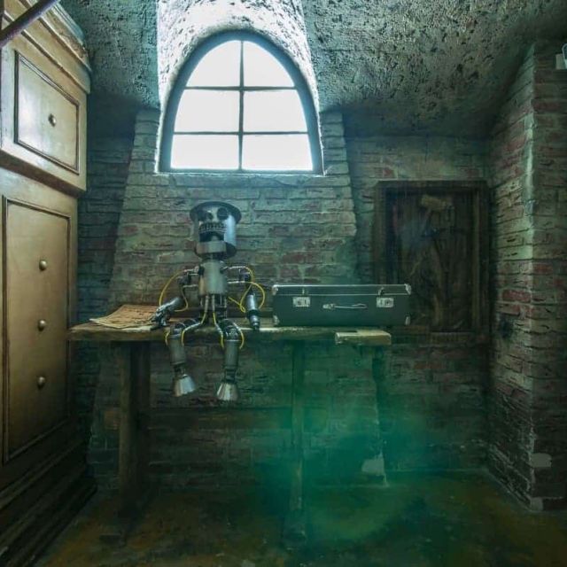 Pièce souterraine aux murs de brique, robot mécanique sur table, fenêtre arquée chez Escape the Cage